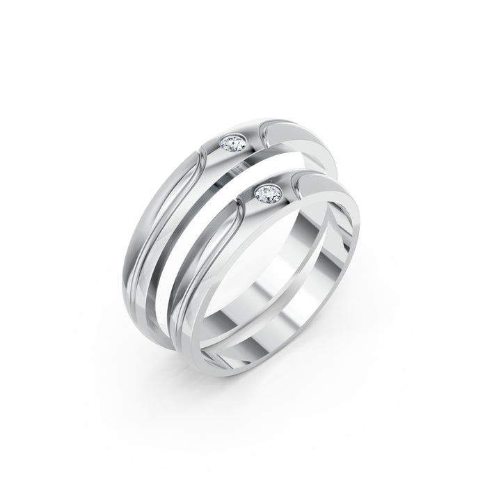 Les Courbes Complices, două verighete cu linii curbe și câte un diamant rotund, metal alb, vedere oblică, verighete suprapuse.